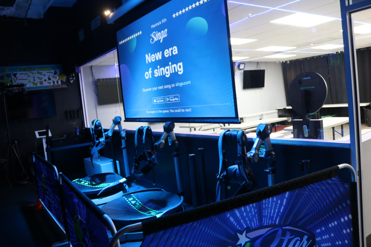 VR racing rig beside karaoke screen at All Star Party World