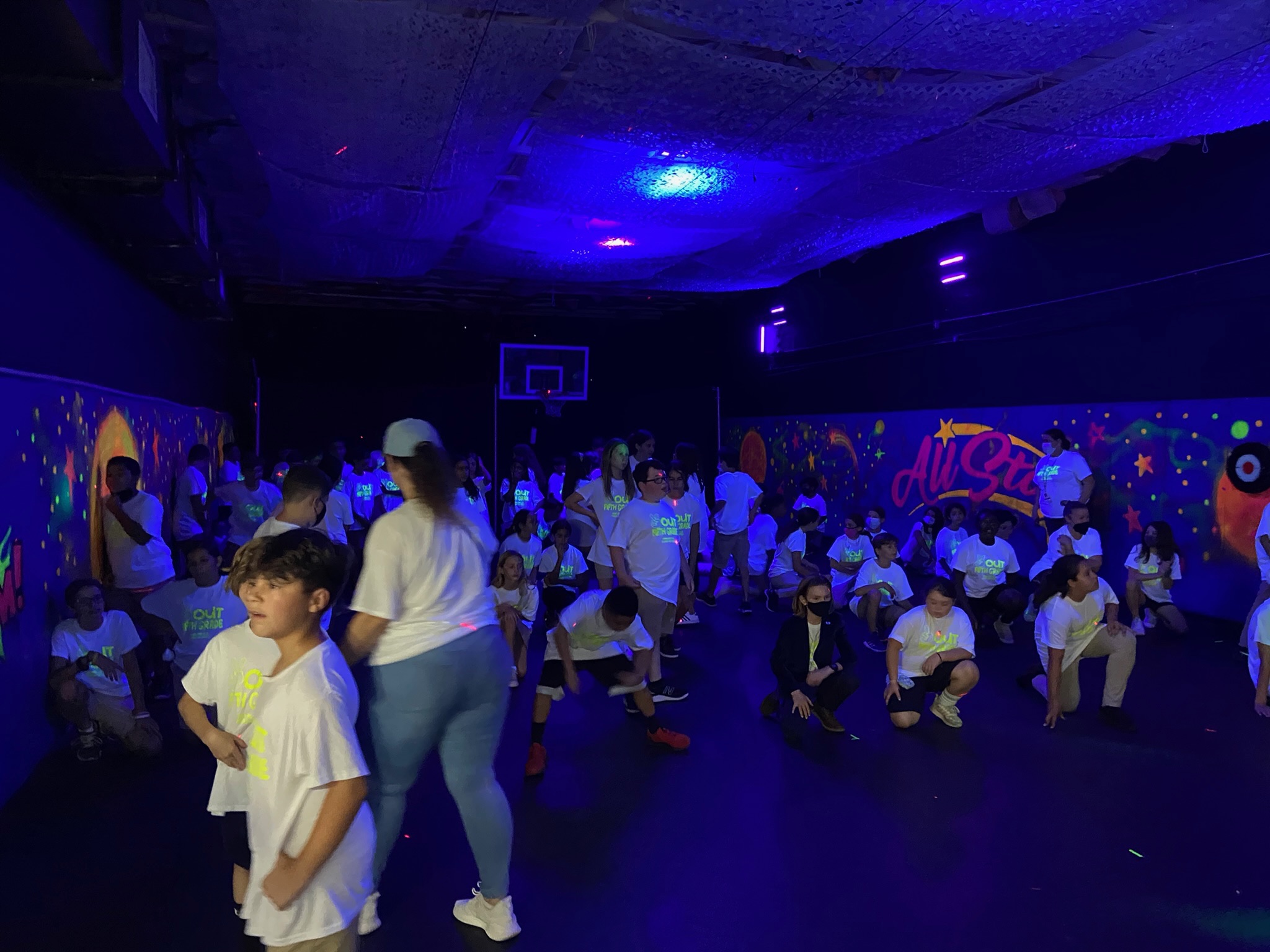 Kids dancing at a glow party under blacklights with All Star Party World mural in background