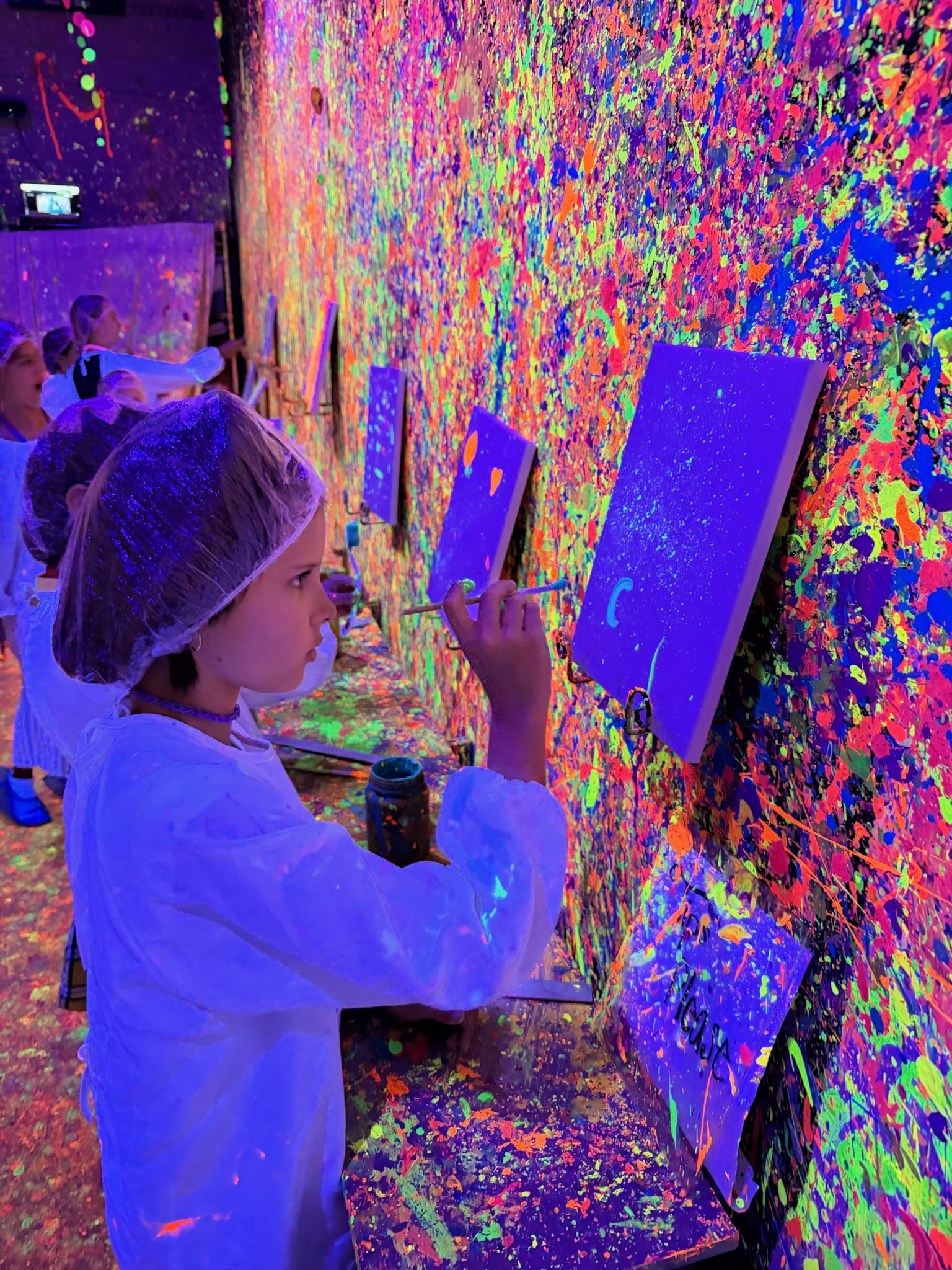 Close-up of a girl painting her canvas with neon paint in the blacklight room