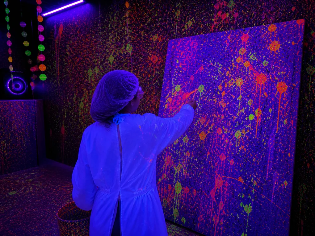 Participant painting on a large canvas in the neon blacklight Paint Me One room